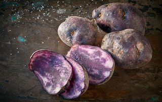 Sliced vitelotte potatos, three slices and three whole potatos on rough dark background