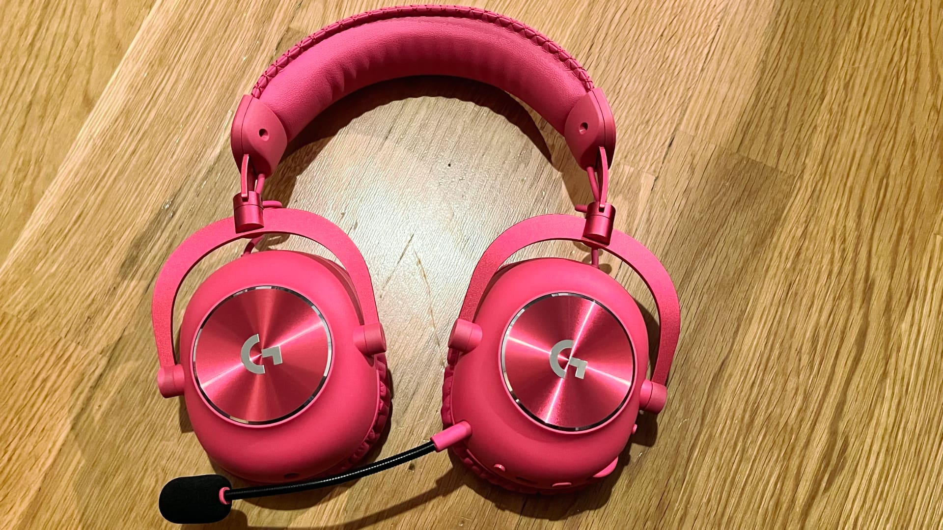 Ett par chockrosa Logitech G PRO X 2 LIGHTSPEED ligger på ett träbord.
