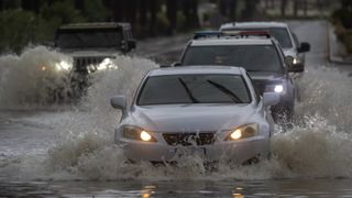 A line of cars drives through a flooded street