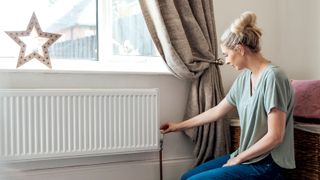 Women turning radiator valve on white radiator under window