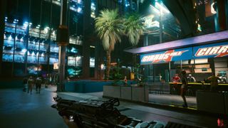 Cyberpunk 2077 gameplay with shopfronts, palm trees, NPCs, and character holding machine gun.