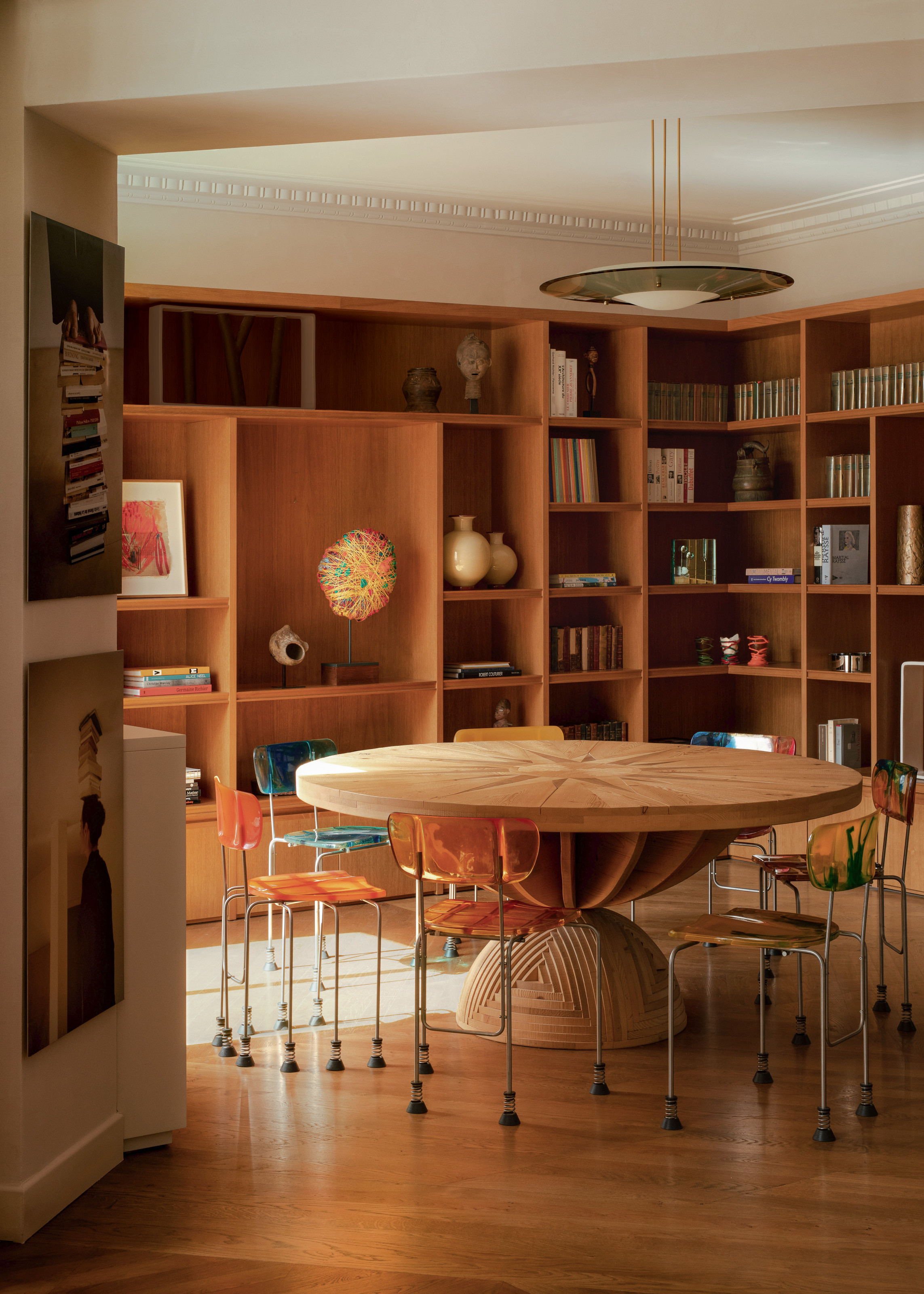 Round office with floor-to-ceiling wood joinery and shelving, wooden floor, large round sculptural wooden table and metal and plastic chairs