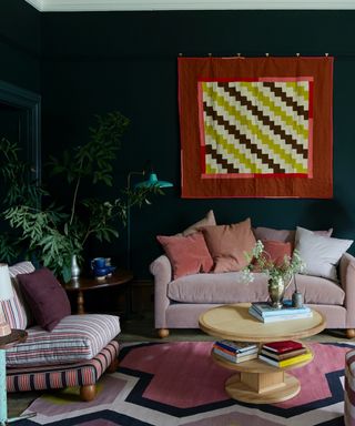 timeless interior design styles, dark blue walls in living room, bright red and yellow wall hanging, pink couch, pink stripe armchair, eclectic coffee table, graphic rug, plants