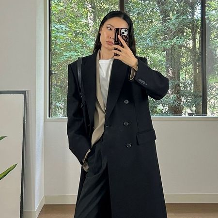 Woman wears white top, black coat, black tailored trousers