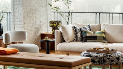 outdoor living area with white ikea stockholm sofa, bench seat, side table with patterned lamp, white boucle armchair, patterned upholstered ottoman with a tray with decor in it