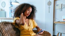 woman rubs neck while scrolling on phone 