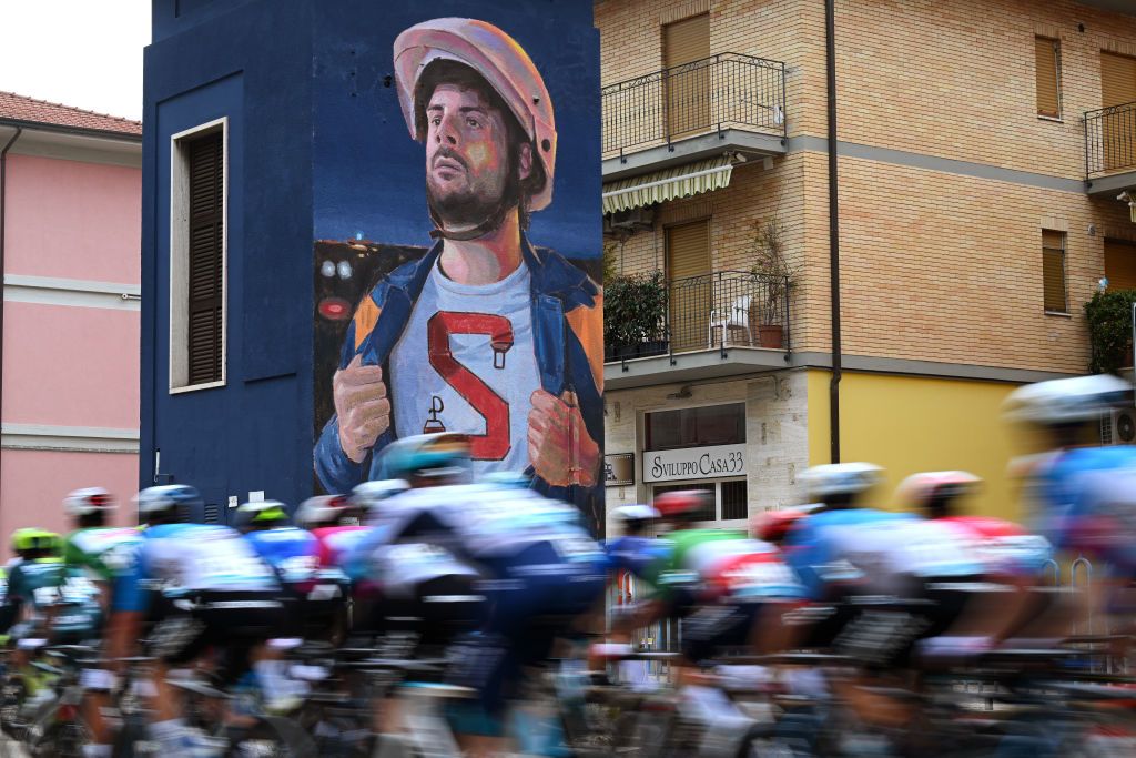 Pack races by a wall mural during stage 7 in San Benedetto del Tronto