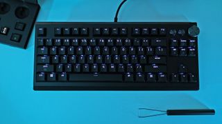 Top-down view of a black Razer Huntsman Signature Edition mechanical keyboard on a blue background, flanked by a keycap puller and extra keycaps.