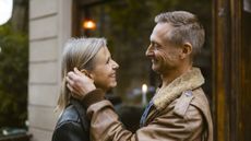 An older, attractive couple looks into each other's eyes outside a restaurant. They look like they are on a date.