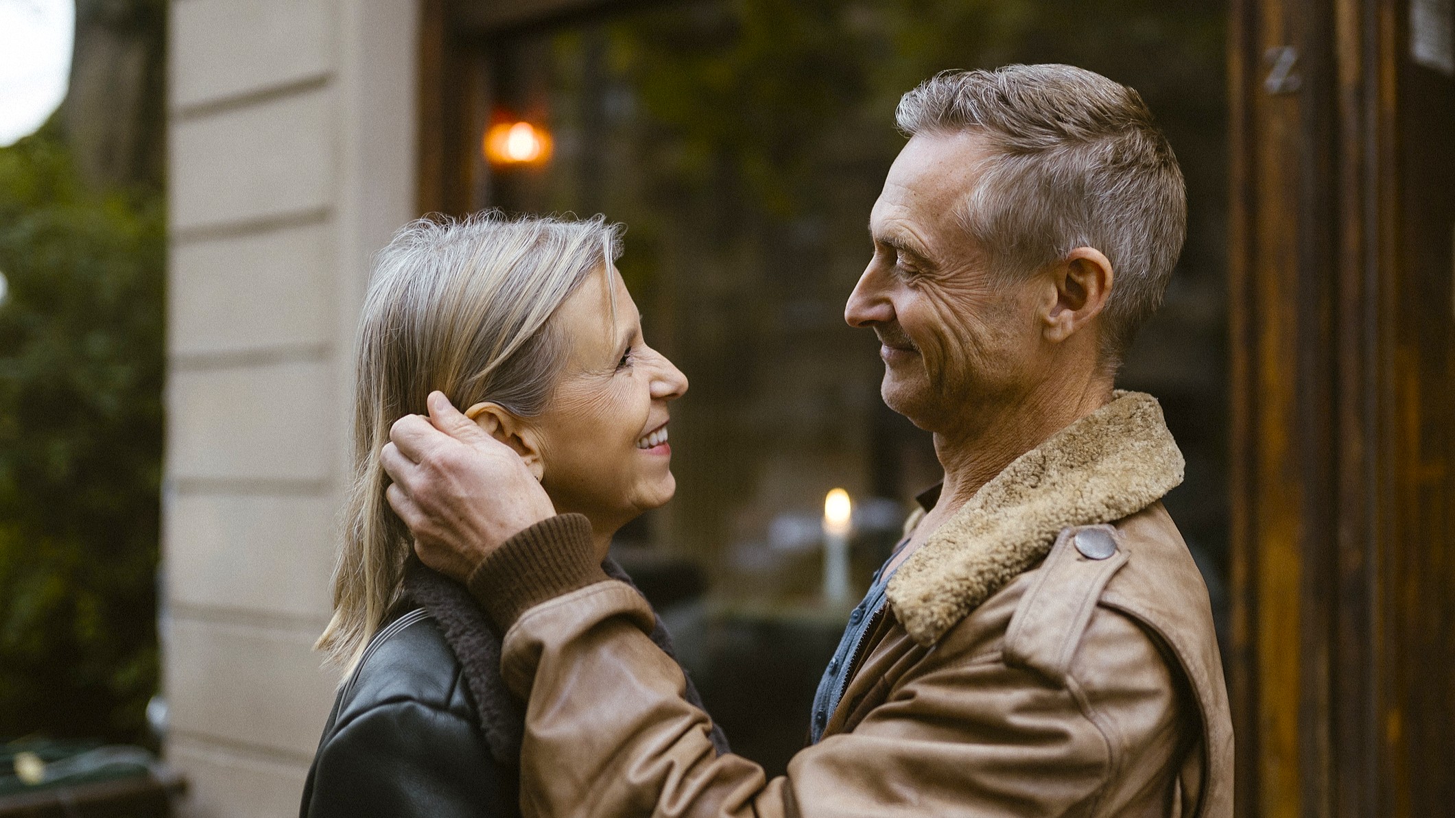 An older, attractive couple looks into each other's eyes outside a restaurant. They look like they are on a date.