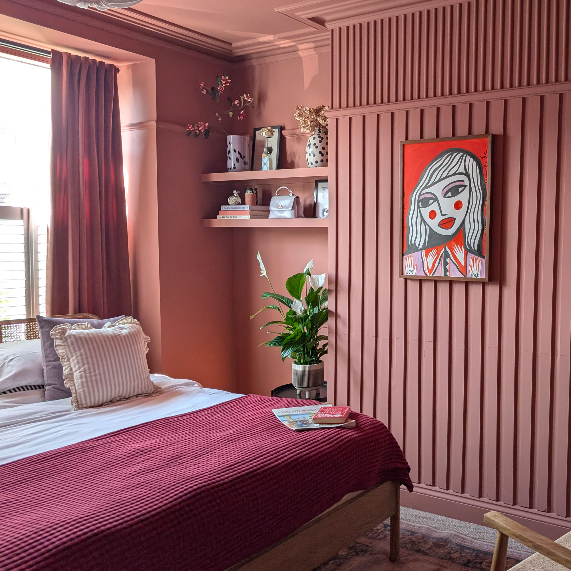 Colour drenched pink bedroom with wall panelling, floating shelves, painted ceiling and bed beneath window
