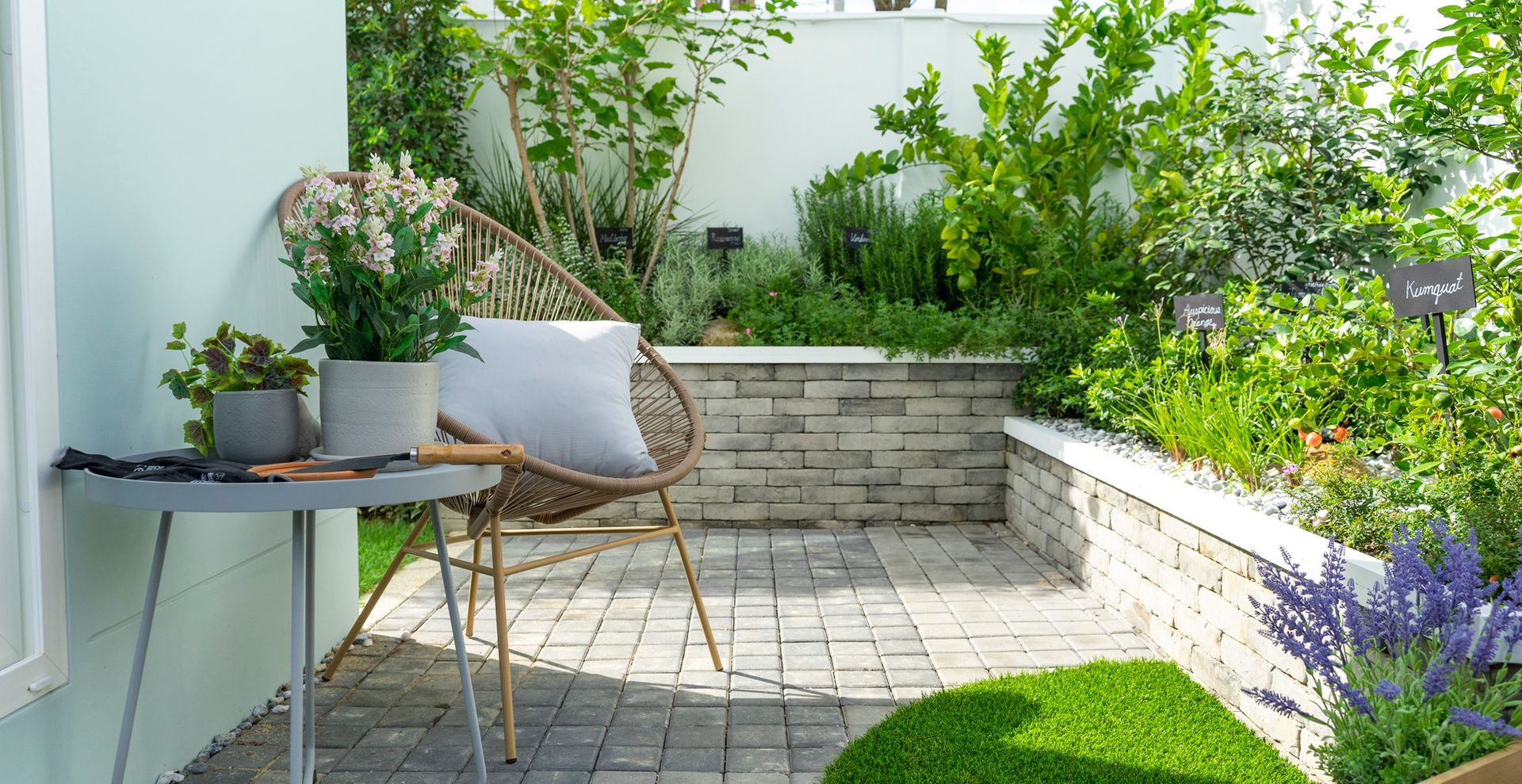 small garden with paved patio area with herb planted border beds and single chair and small table