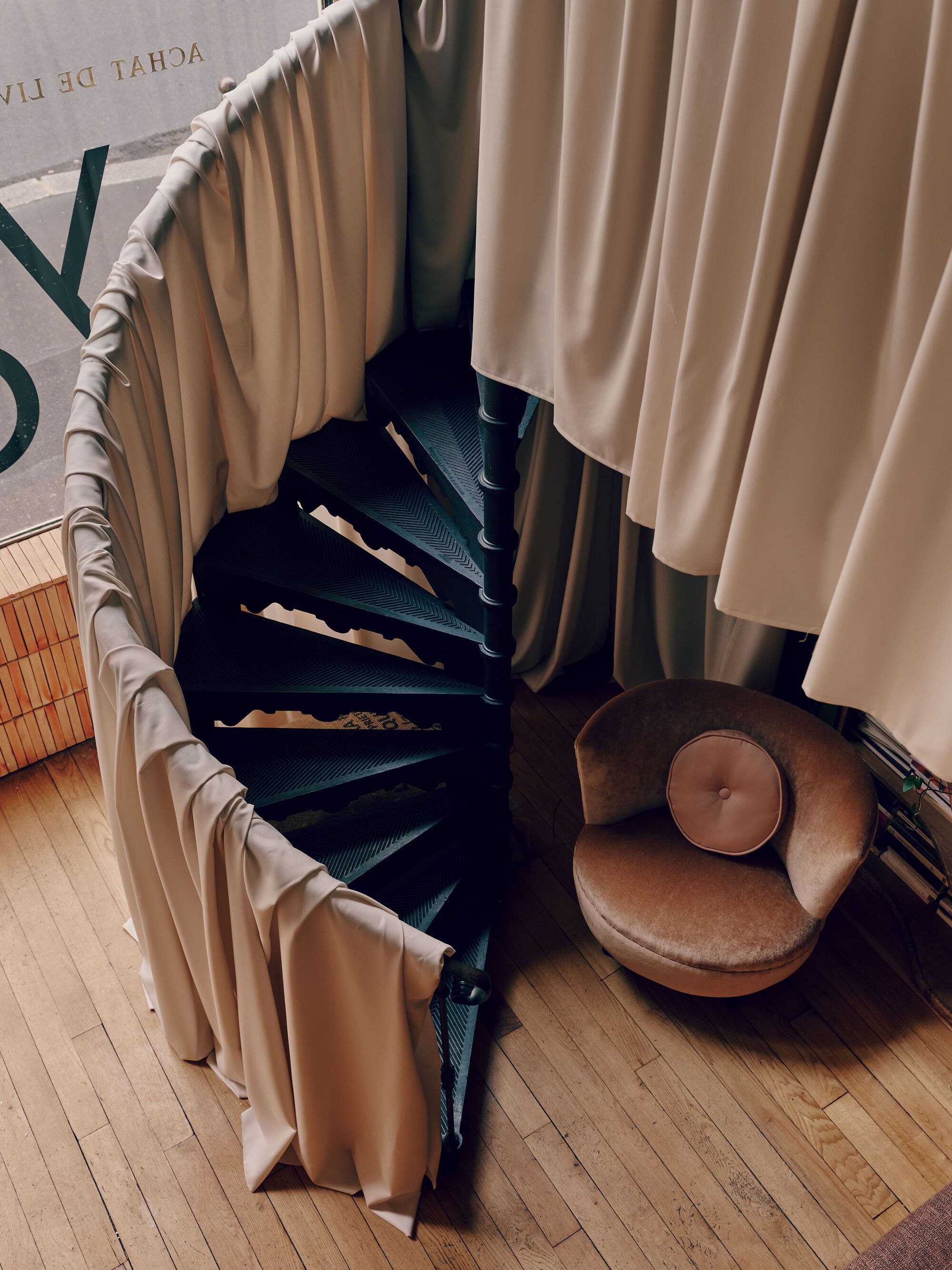 Image from above of a black spiral staircase covered in a cream fabric with a caramel velvet accent chair at the bottom.