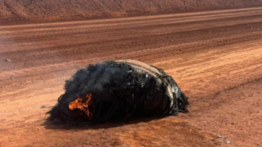 A photo of a smoking black wreckage on red sand 