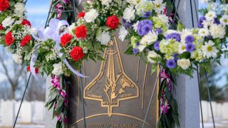 a bronze memorial marker inscribed with a mission patch in the shape of a space shuttle with flower wreaths atop it