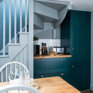Light blue kitchen with dark blue green breakfast nook under stairs