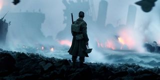 Tommy holds his helmet at his side as he watches debris burn in the distance in 'Dunkirk'