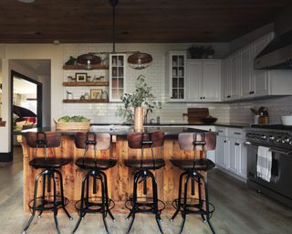 kitchen with wooden island, wood and metal bar stools, industrial style light and white cabinets and backsplash tile