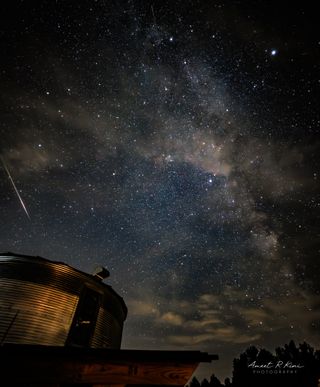 射擊星是一張照片,沿著夜空衝入了金屬筒倉上方的銀河系閃閃發光的樂隊旁邊。