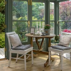 A green conservatory with a corner adorned with mismatched vintage table and two chairs