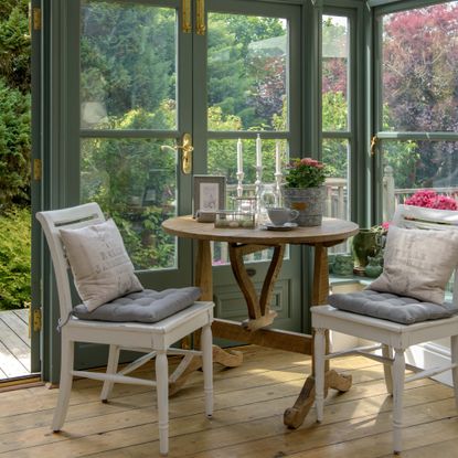 A green conservatory with a corner adorned with mismatched vintage table and two chairs