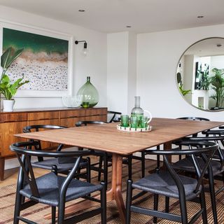 dining area with wooden dining table and chairs and white wall with round mirror