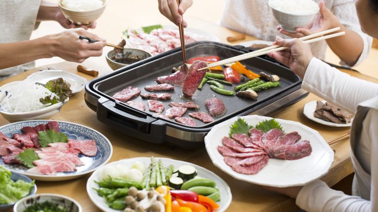 An oriental family enjoying a Japanese meal of grilled meats on electric Yakiniku grill