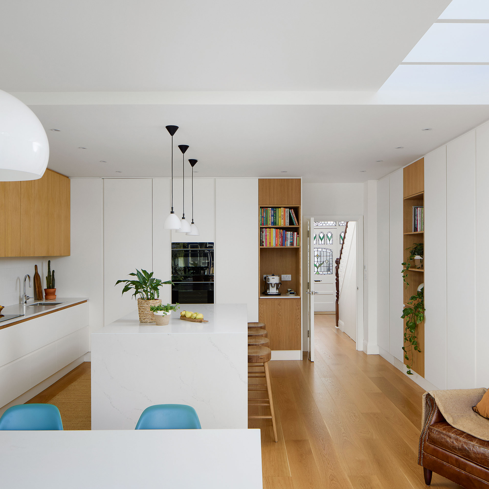 White kitchen with wooden floor, sleek cabinetry and white island