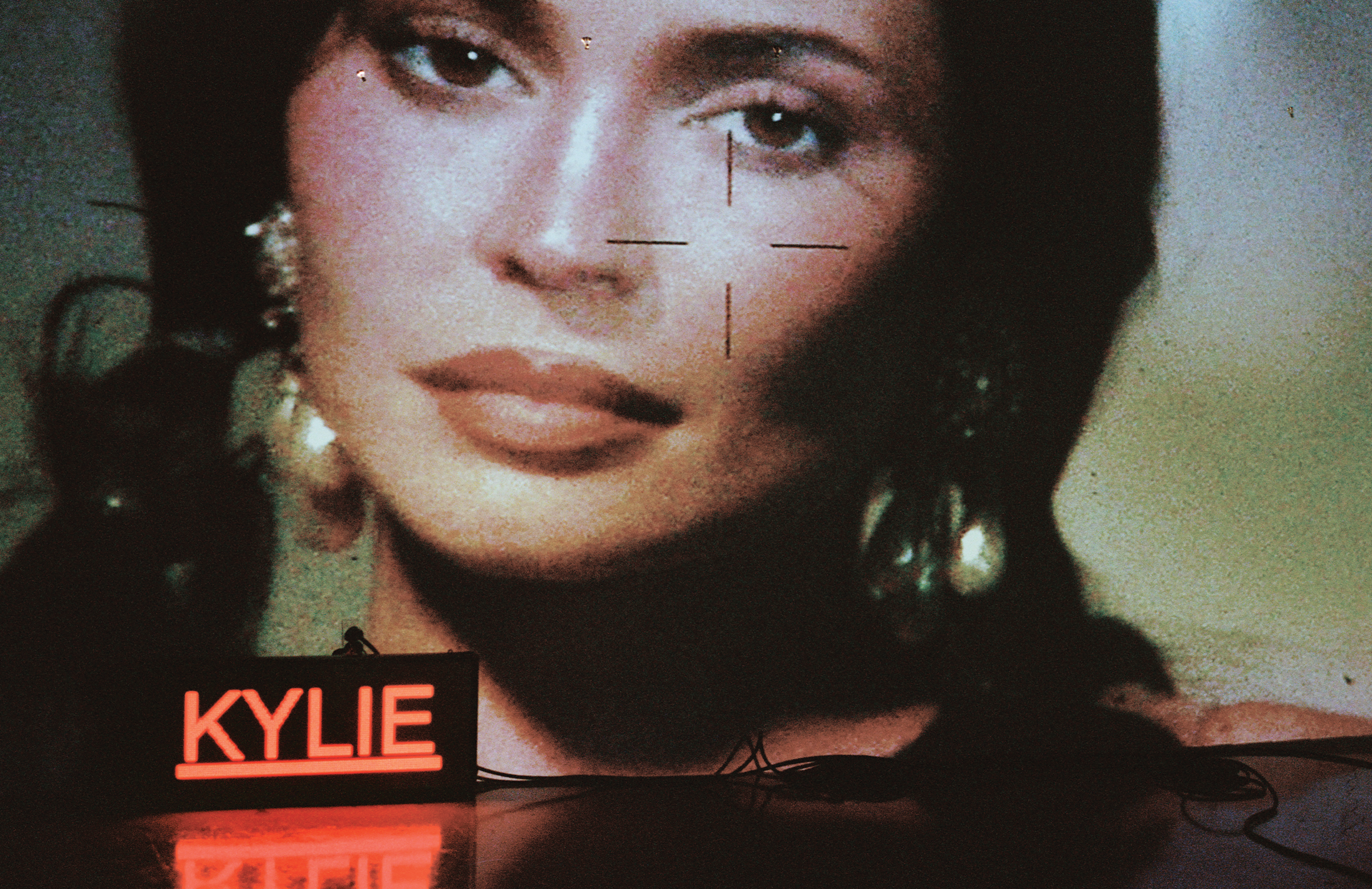 Kylie Jenner is projected on the wall with a neon sign with her name on the floor.