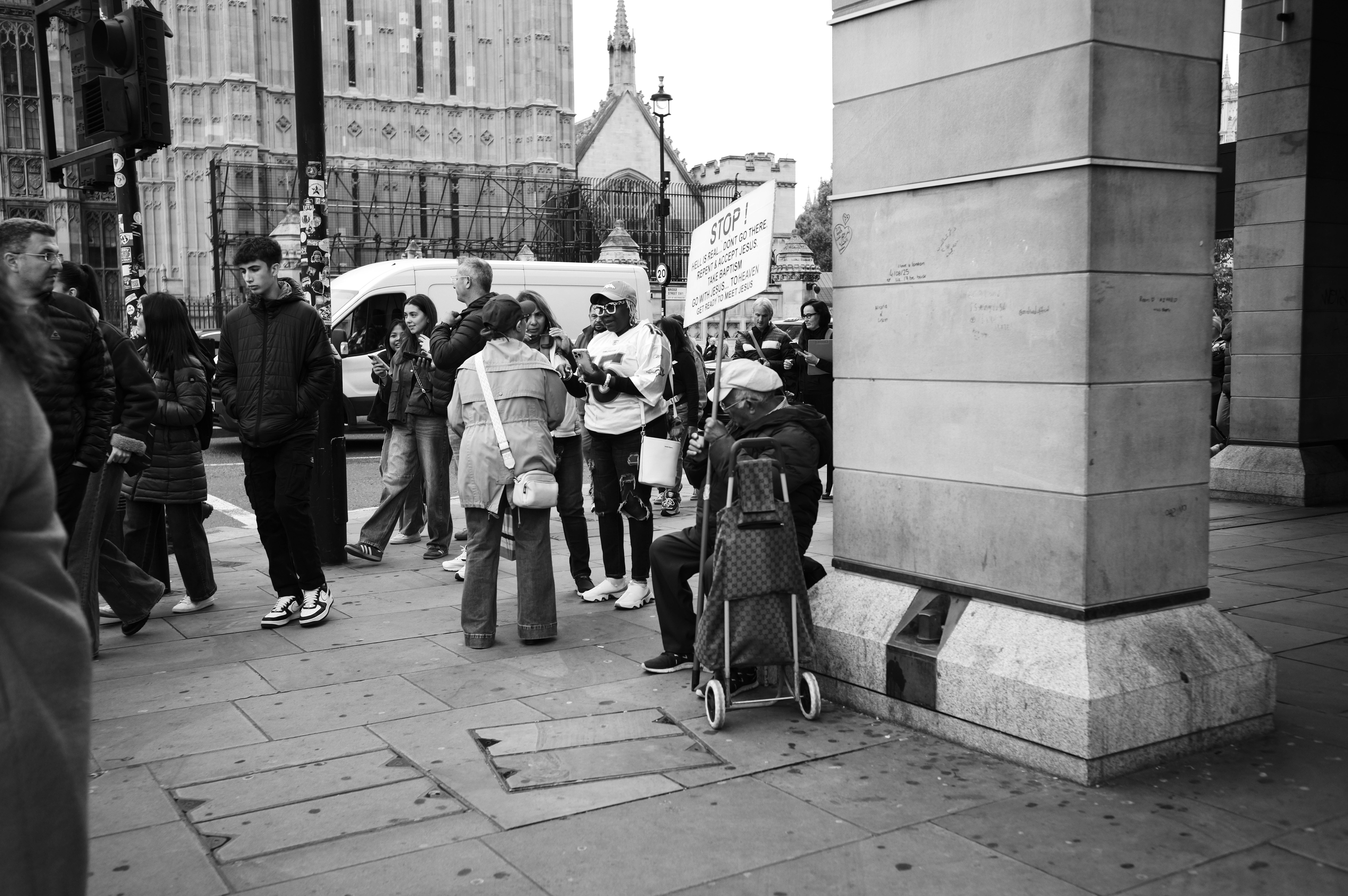 Person sitting on a street corner holding a sign surrounded by a crowd
