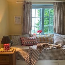 window seat in a pale yellow room covered with a gingham throw and a variety of check cushions