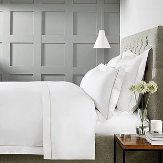 A side view of a bed with crisp white bedding and a grey panelled wall behind