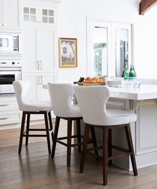 All white kitchen in light and bright space, kitchen island, piece of artwork adding warmth and character to the space