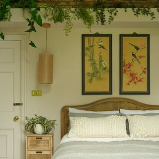 a large main bedroom decorated in a neutral scheme with an exposed brick wall, rattan headboard, Asian-style framed prints and plenty of houseplants