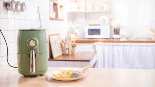 A green air fryer on an open counter next to a plate of French fries