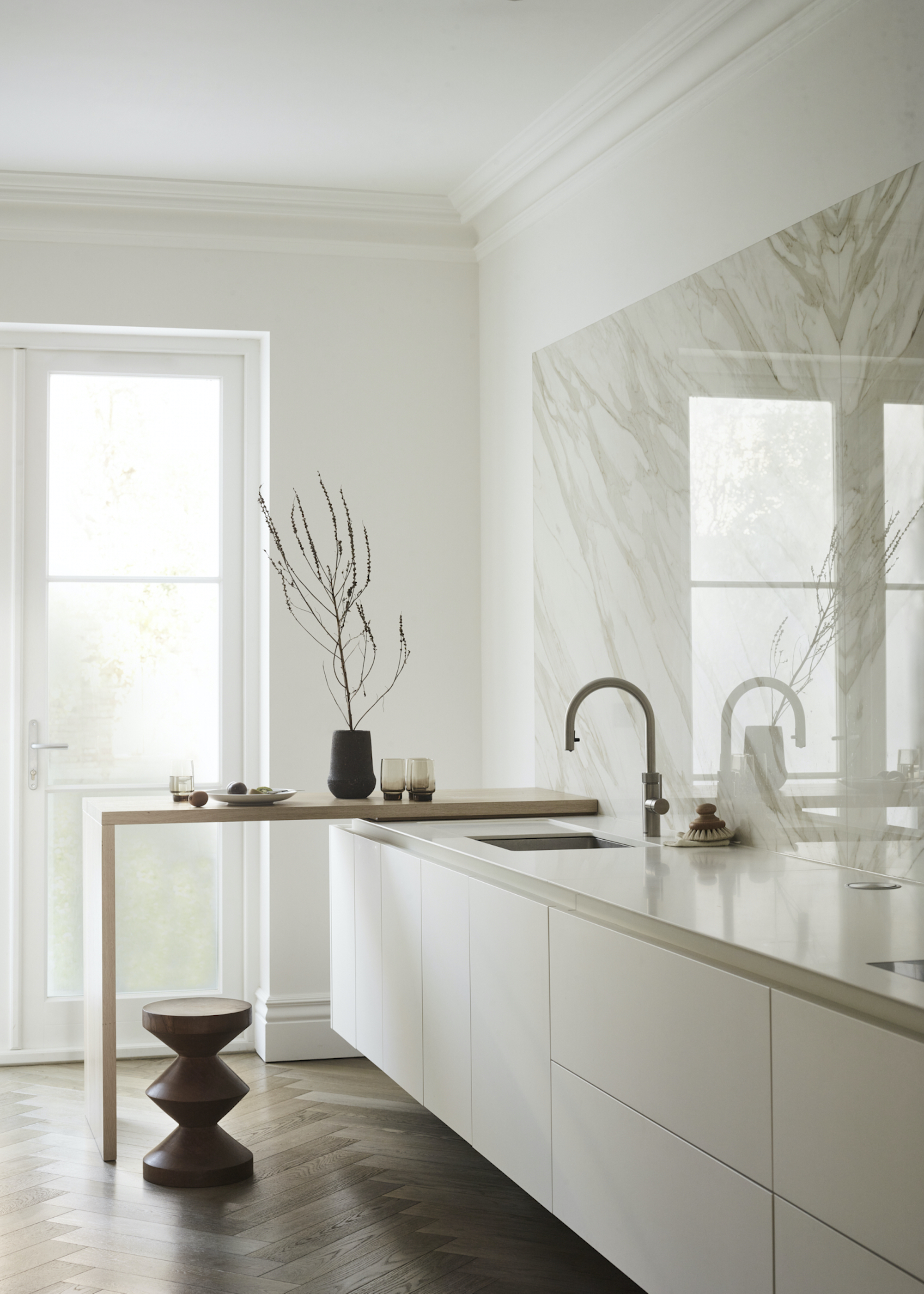white kitchen with an offset bar on the side of the kitchen counter. The bar has a vase and glassware on top.
