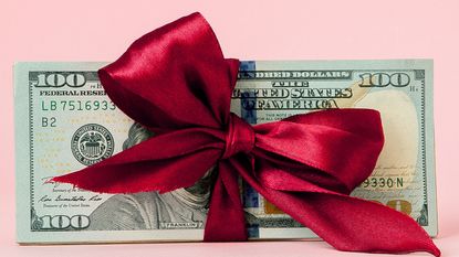 A red bow is tied around a stack of hundred-dollar bills.