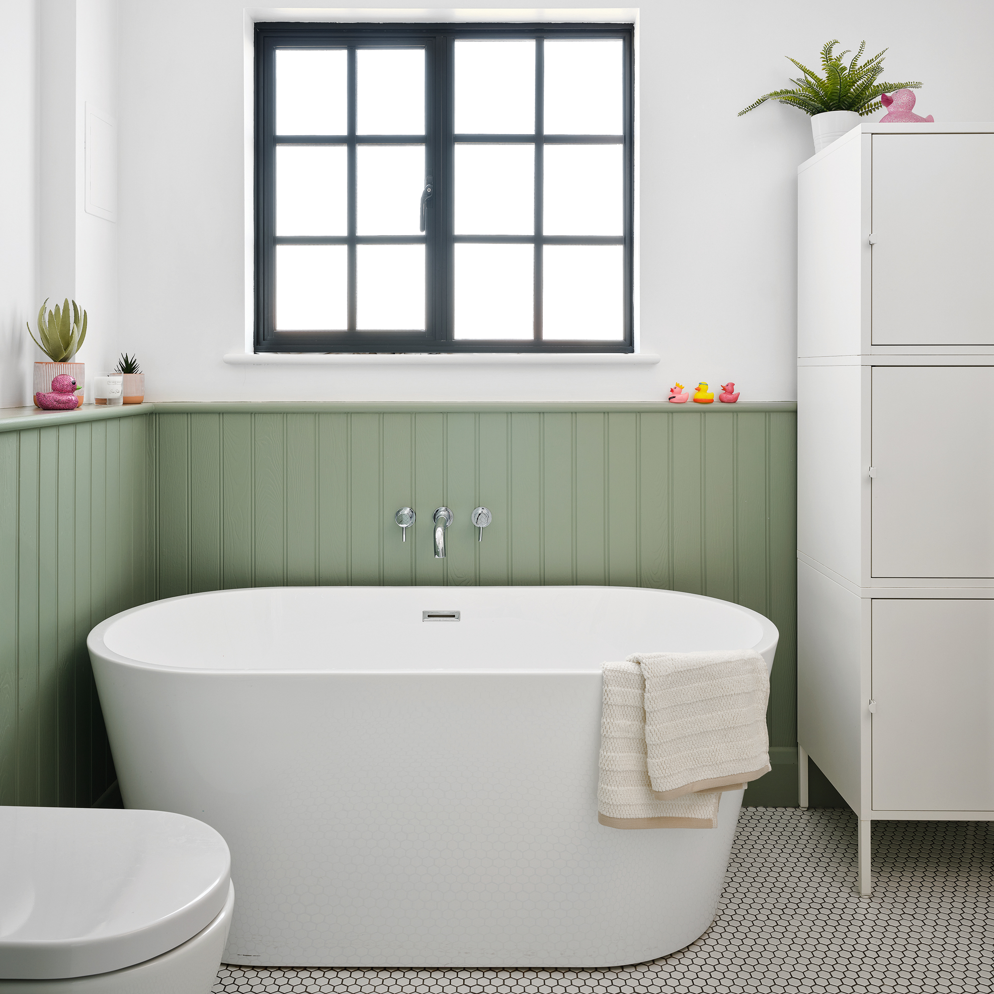 a green and white bathroom with painted green panelling, a large contemporary freestanding bath tub with white micro tiled flooring and a green floating vanity unit