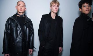 3 models in dark clothing standing in a studio