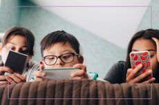 three kids lying on bed using phones