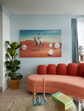 Living room with pale blue walls, canvas painting of person on horse, and two-tone coral-colored sofa