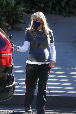 Jennifer lawrence wears a mask, white long-sleeve shirt, graphic t-shirt, and black adidas track pants.