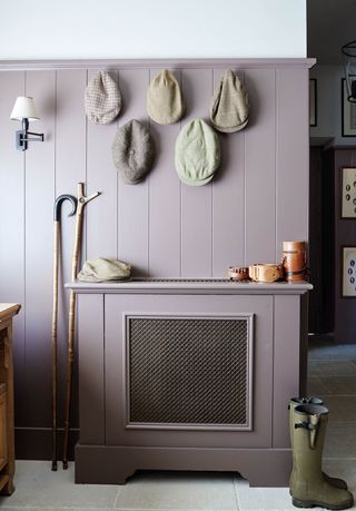 Purple wood paneled walls in a mudroom with wellies on the floor and hats hung on the wall