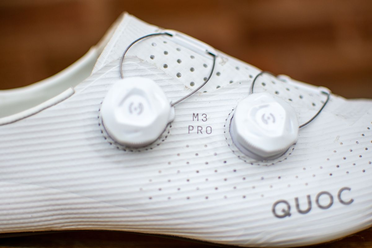 A white Quoc M3 Pro cycling shoe on a wooden chair