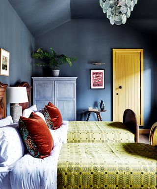 Bedroom with twin wooden beds, dark gray wall, yellow blankets, rust velvet cushions, a yellow door and yellow blankets