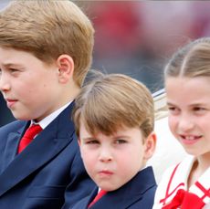 Prince George and Prince Louis wearing blue suits and red ties and Princess Charlotte wearing a red-and-white dress with a red bow riding in a carriage