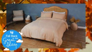 A bed dressed in beige sheets on a wooden bed frame with rattan headboard in bedroom with blue wall and bedside chair on a background of autumnal leaves and Tom's Guide's Fall Back into Great Sleep campaign logo 