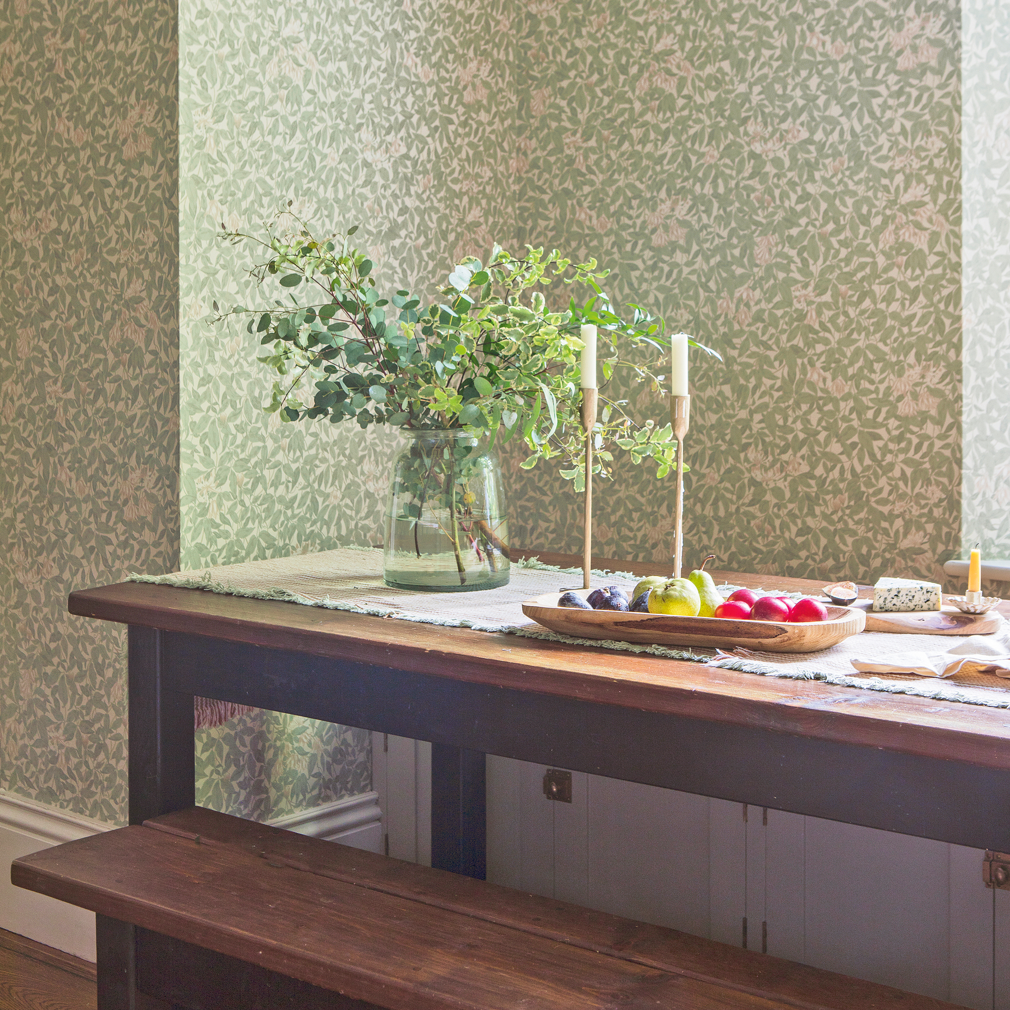 a dining room with a wooden dining table with a vase of flowers and two candlesticks