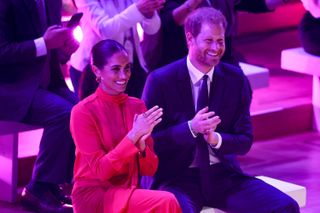 Prince Harry and Meghan Markle clap as they sit next to each other
