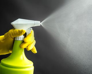 Woman wearing yellow rubber gloves using green spray bottle and spraying liquid mist in air, cool lighting effect